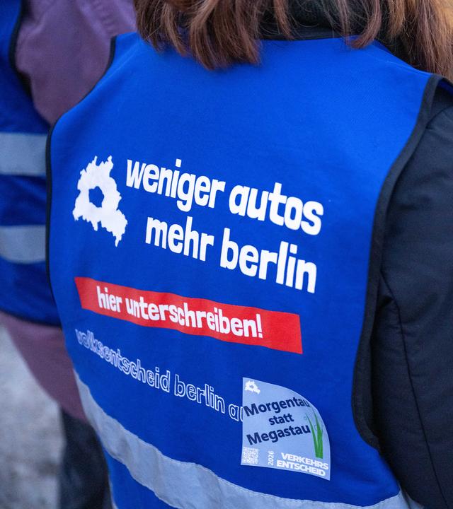 Der Rücken einer Person, die ein blaues Leibchen mit der Aufschrift "weniger autos - mehr berlin - hier unterschreiben!" trägt.
