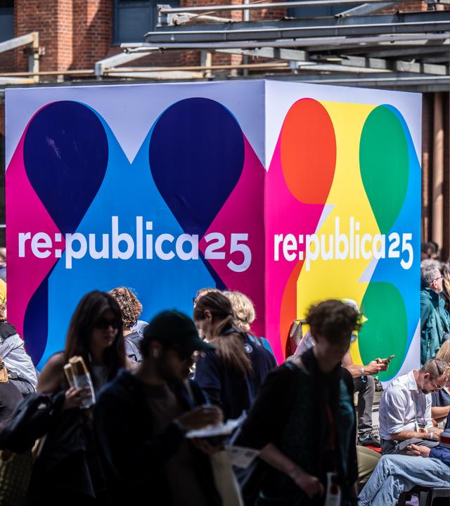 Besucher der Medienkonferenz Re:publica sitzen an einem Logo-Aufsteller am Veranstaltungsort «Station Berlin»