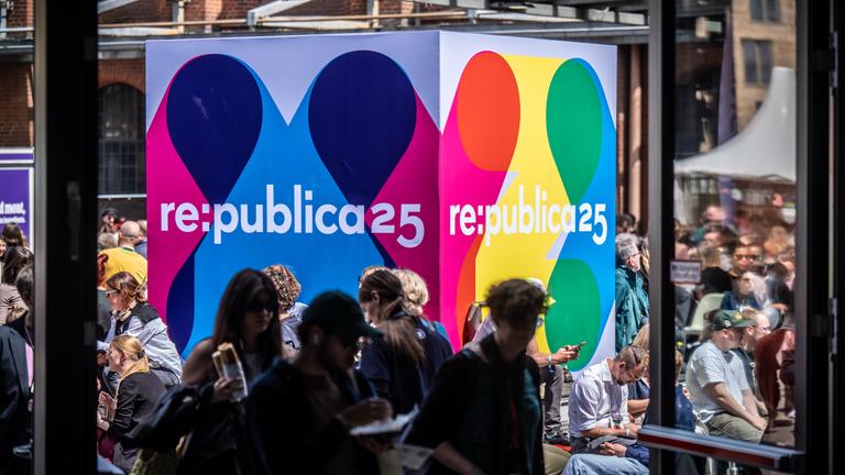 Besucher der Medienkonferenz Re:publica sitzen an einem Logo-Aufsteller am Veranstaltungsort «Station Berlin»