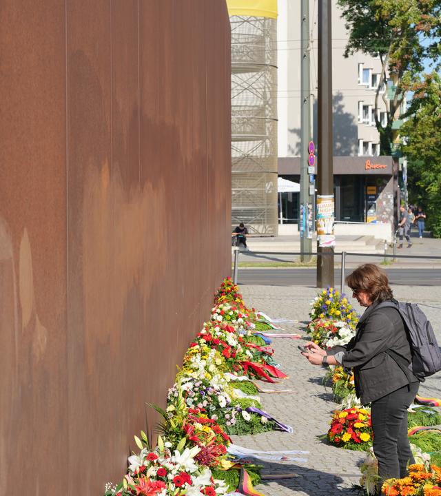 Eine Frau steht vor Beginn der Gedenkfeier zum 65. Jahrestag des Mauerbaus vor den Kränzen an der Gedenkstätte Bernauer Straße. 