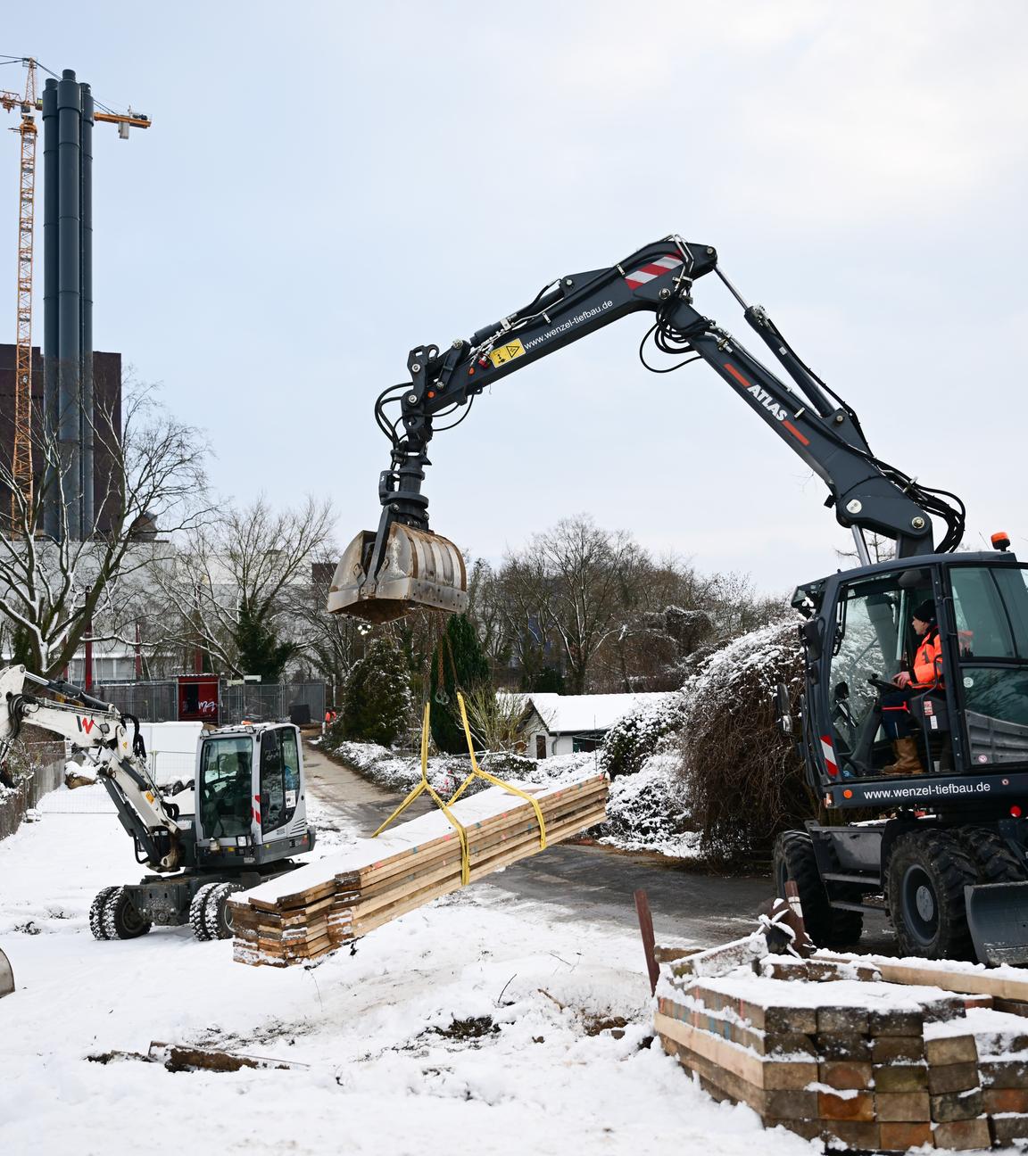 Ein Bagger nimmt während eines Stromausfalls im Südwesten Berlins vor der ausgebrannten Kabelbrücke Balken für die Baustelle auf.