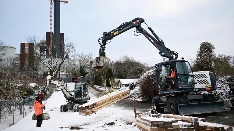 Ein Bagger nimmt während eines Stromausfalls im Südwesten Berlins vor der ausgebrannten Kabelbrücke Balken für die Baustelle auf.