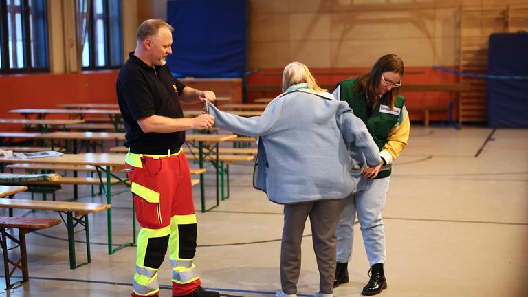 Helfer bringen eine ältere Frau während eines Stromausfalls in eine Notunterkunft in einer Schulturnhalle im Südwesten Berlins, Deutschland, 5. Januar 2026.