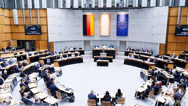 Der Plenarraum des Berliner Abgeordnetenhaus während einer Plenarsitzung. An der Wand hängen drei Flaggen: Deutschland, das Land Berlin und die EU.