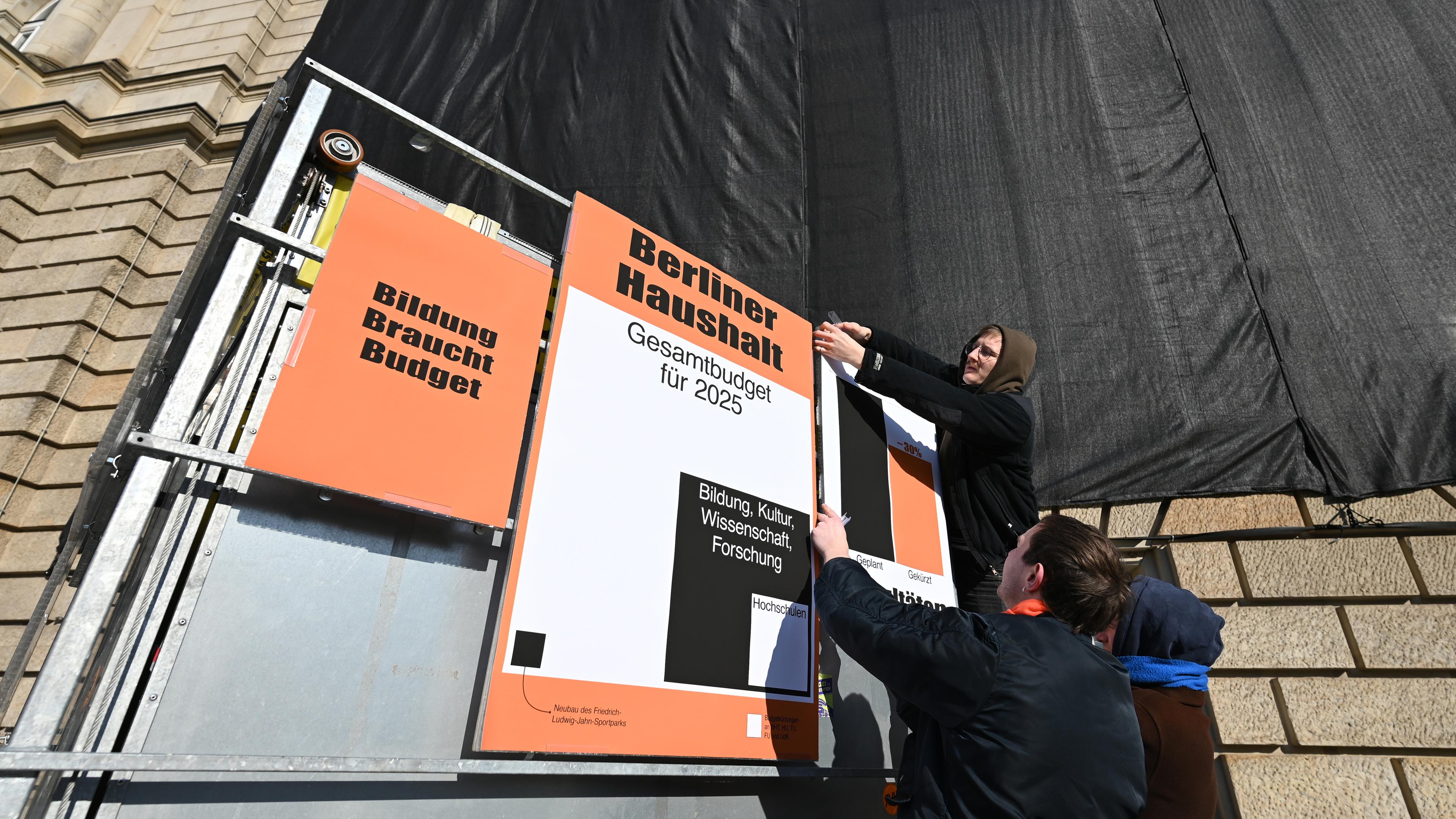 Ein Student hängt Protestplakate gegen Haushaltskürzungen der Unis in Berlin auf.