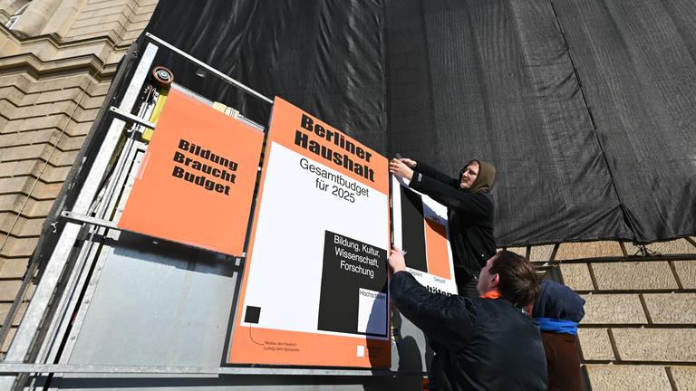Ein Student hängt Protestplakate gegen Haushaltskürzungen der Unis in Berlin auf.