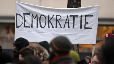 Menschen ziehen während einer Demonstration an einem Banner mit der Aufschrift «Demokratie» vorbei.