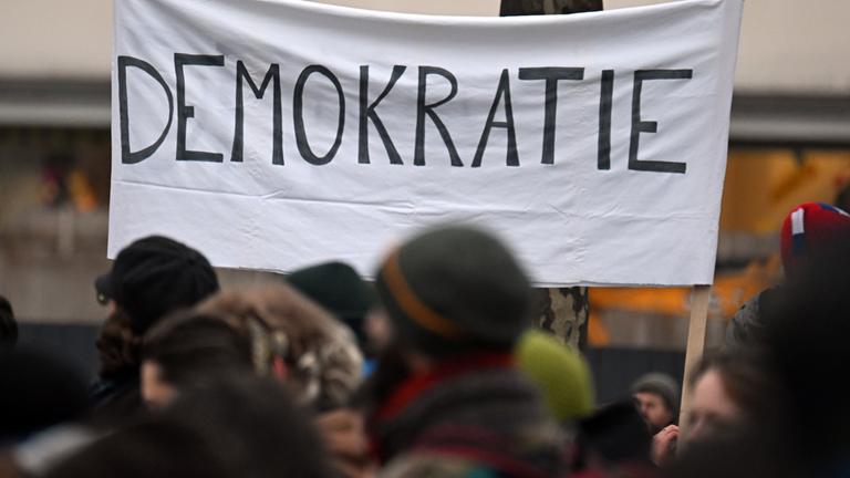 Menschen ziehen während einer Demonstration an einem Banner mit der Aufschrift «Demokratie» vorbei.