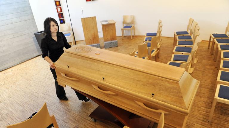 Eine Auszubildende schiebt einen Sarg aus einer Aussegnungshalle.