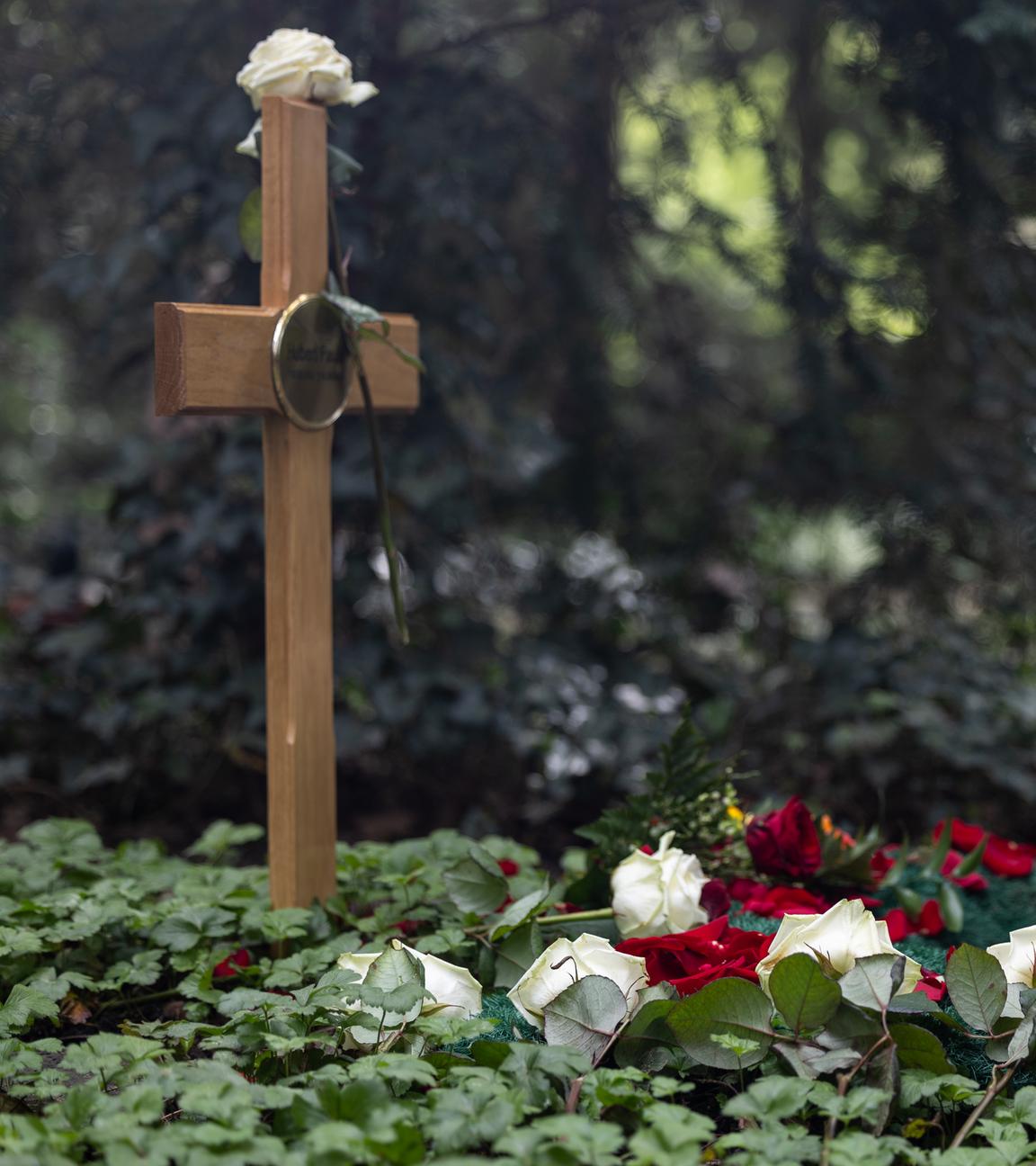 Ein Grab mit Holzkreuz, verziert mit Rosen zum Abschied.