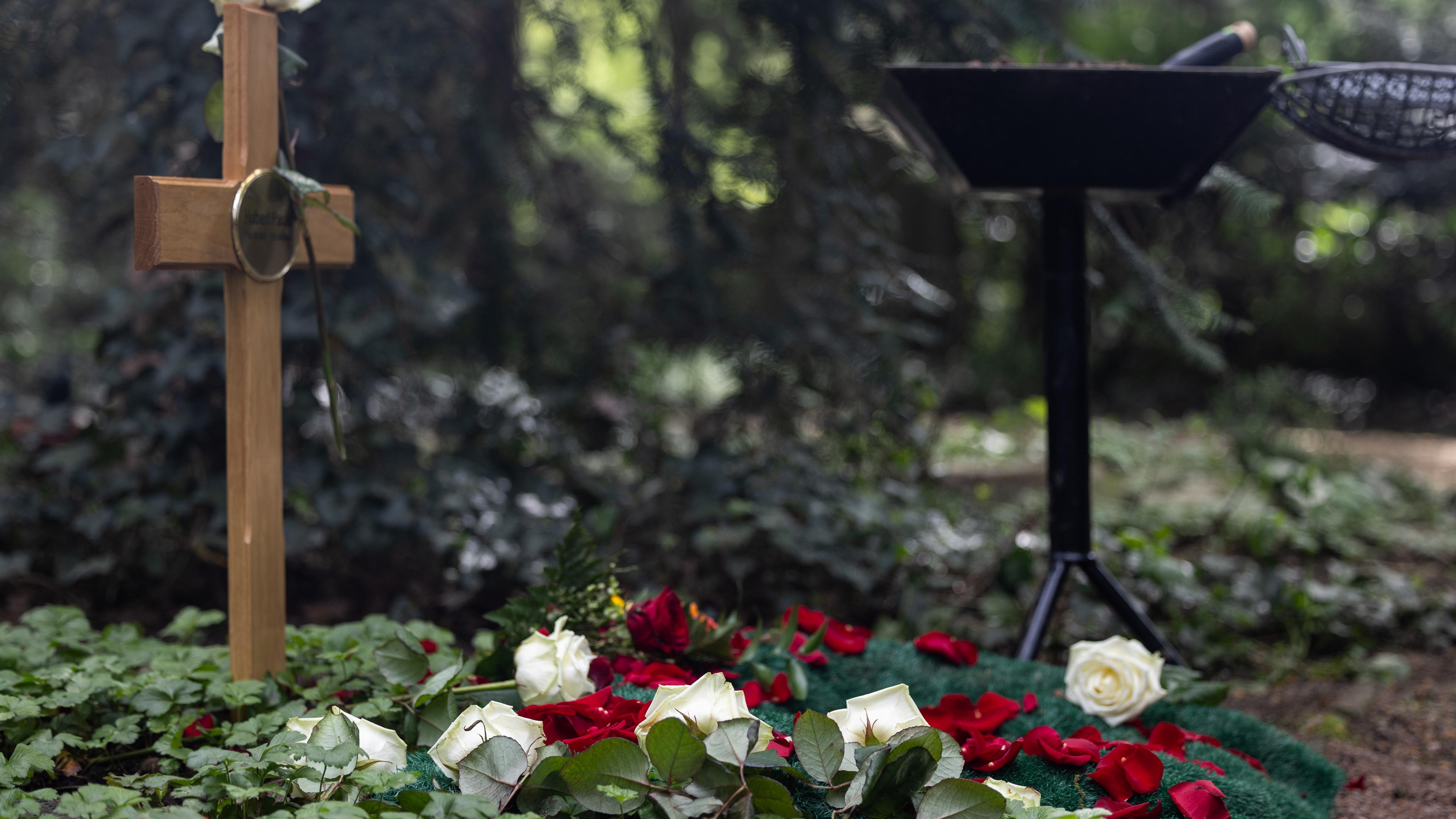 Ein Grab mit Holzkreuz, verziert mit Rosen zum Abschied.