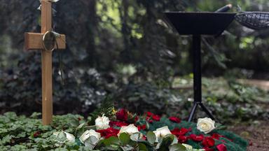 Ein Grab mit Holzkreuz, verziert mit Rosen zum Abschied.