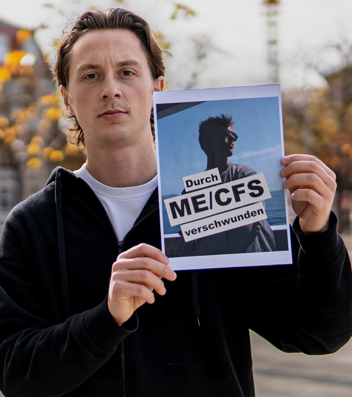 Jonas hält ein Bild von seinem besten Freund, Tom mit dem Schriftzug "Durch ME/CFS verschwunden" in der Hand und zeigt es in die Kamera