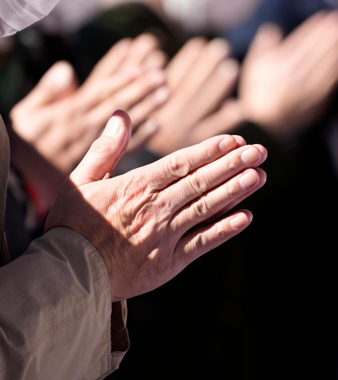 Betende Hände von mehreren Menschen, die in einer Reihe stehen.