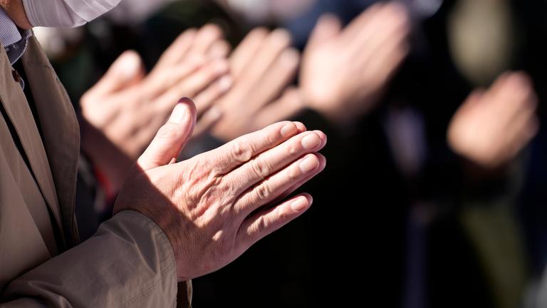 Betende Hände von mehreren Menschen, die in einer Reihe stehen.