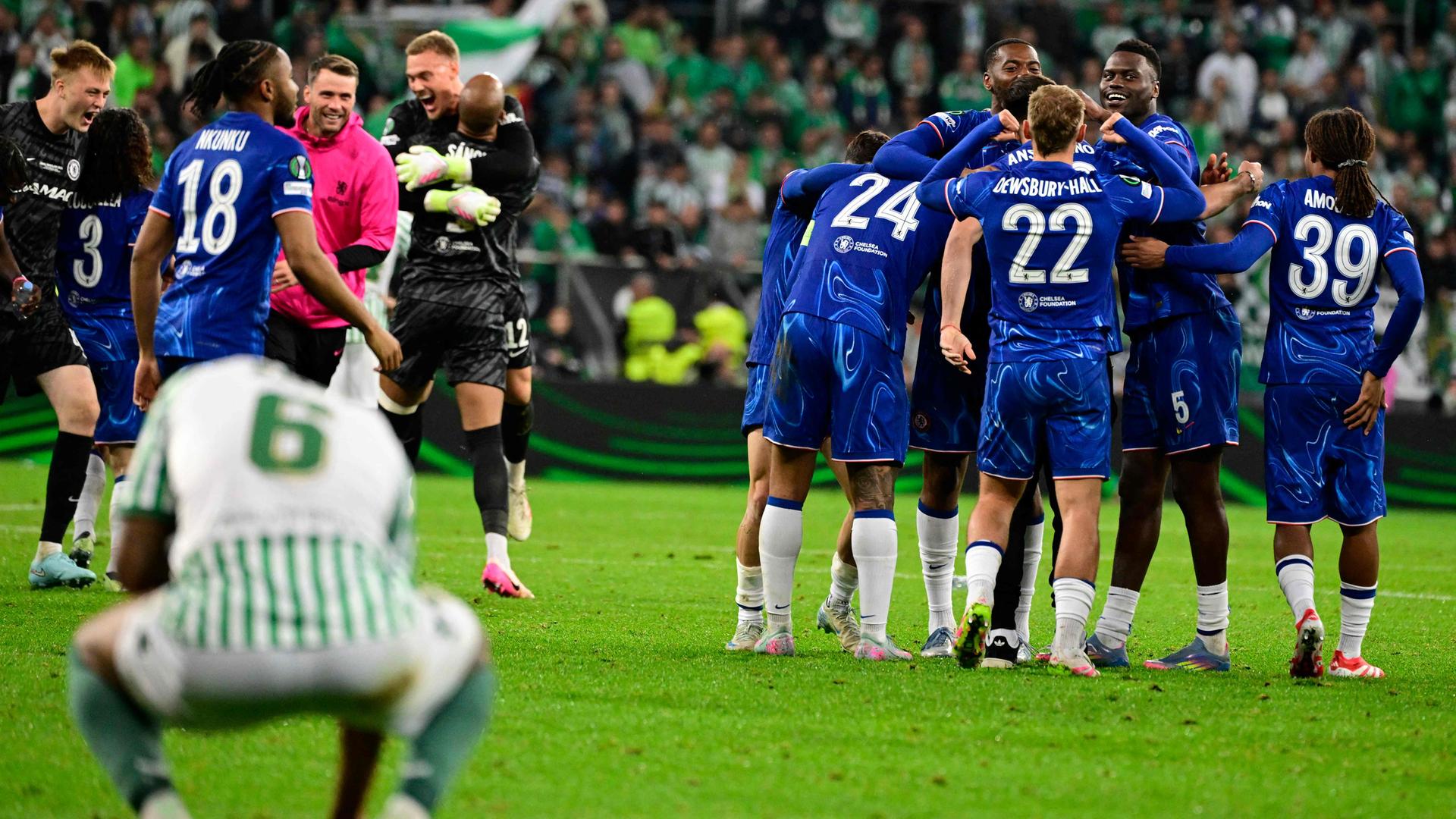 Im Vordergrund kniet ein Betis-Spieler, während im Hintergrund die Spieler des FC Chelsea in einer Jubeltraube feiern.