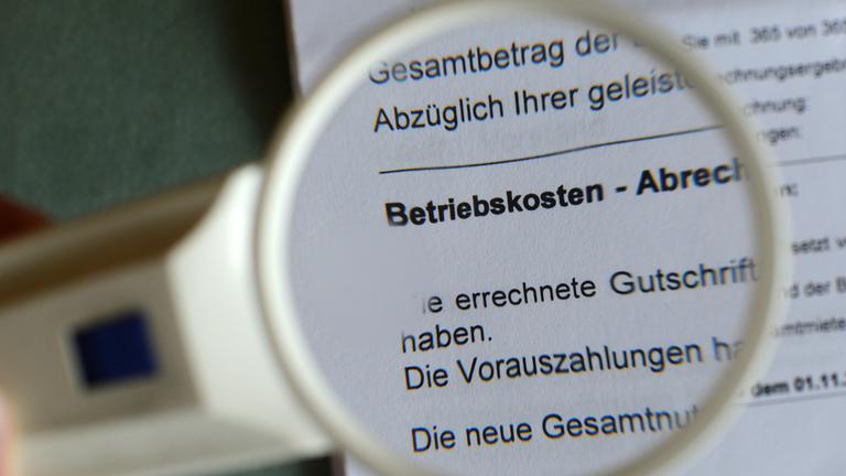 Durch eine Lupe ist ein Dokument der Betriebskostenabrechnung zu sehen.