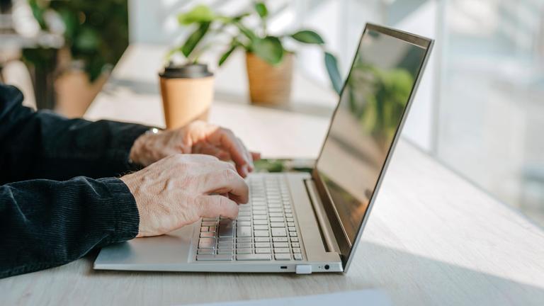 Hand eines Mannes tippt auf Laptop-Tastatur.