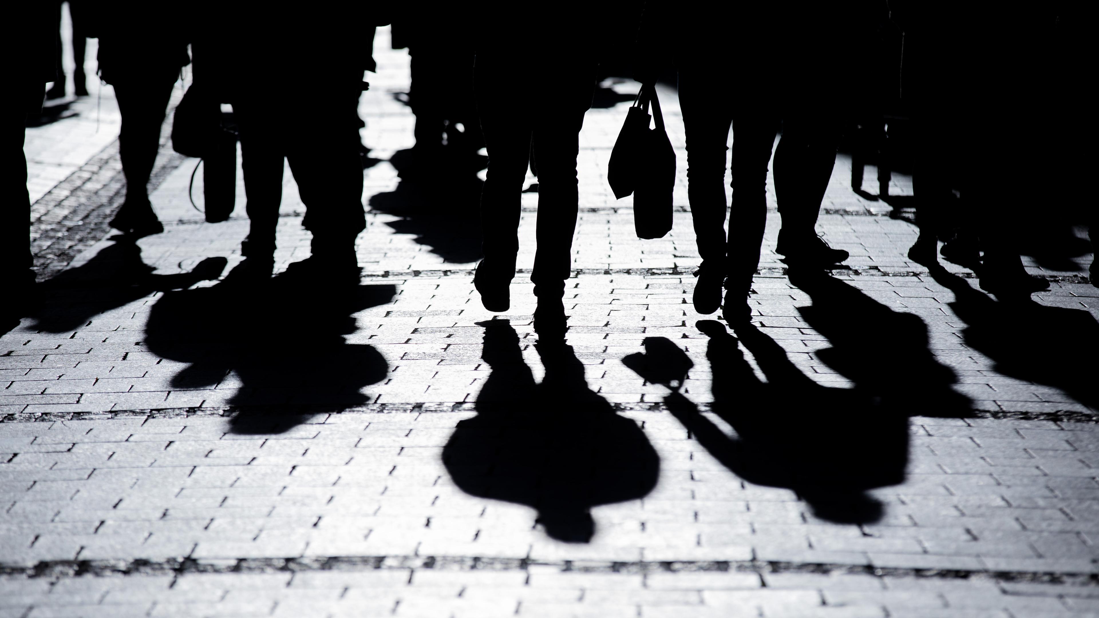 Menschen gehen in starkem Gegenlicht mit ihren Einkäufen durch die Innenstadt