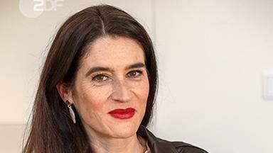 Sina Mainitz steht an einem Tisch. Schrift "Bezahlen im Urlaub: am liebsten bar"