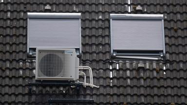 Eine Klimaanlage ist am Dach eines Wohngebäudes unter Dachfenstern zu sehen