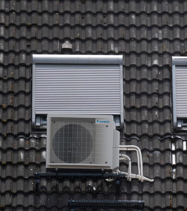 Eine Klimaanlage ist am Dach eines Wohngebäudes unter Dachfenstern zu sehen