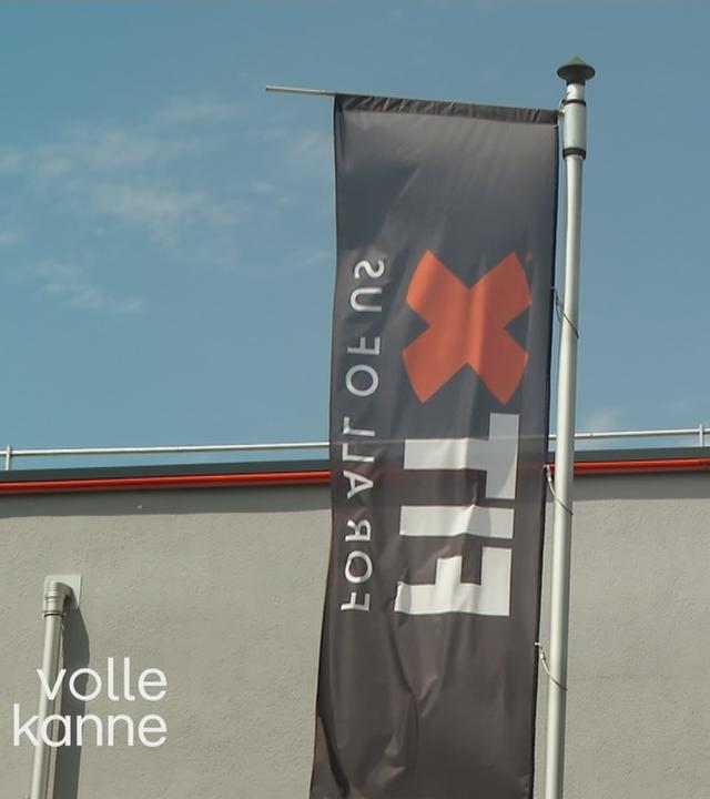 Das Bild zeigt zwei im Wind wehende FitX-Fahnen vor einem Fitnessstudio.