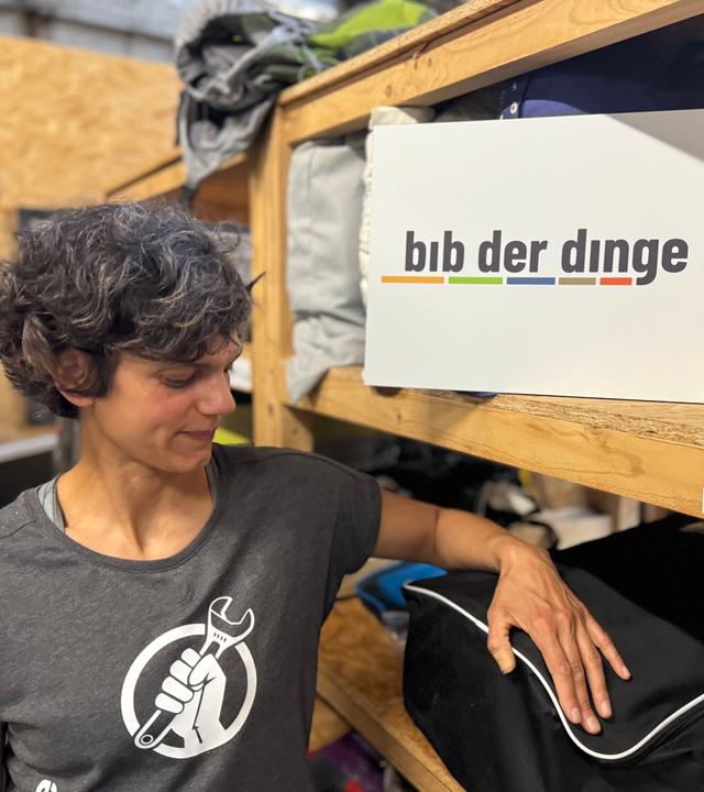 Najine Ameli steht vor einem Regal, in dem ein Schild mit dem Schriftzug "bib der dinge Bochum" steht.