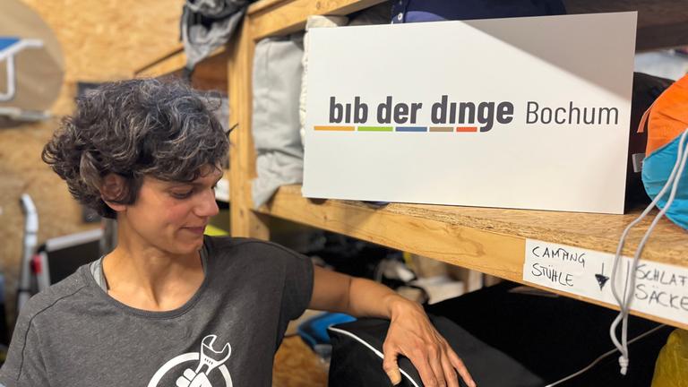 Najine Ameli steht vor einem Regal, in dem ein Schild mit dem Schriftzug "bib der dinge Bochum" steht.