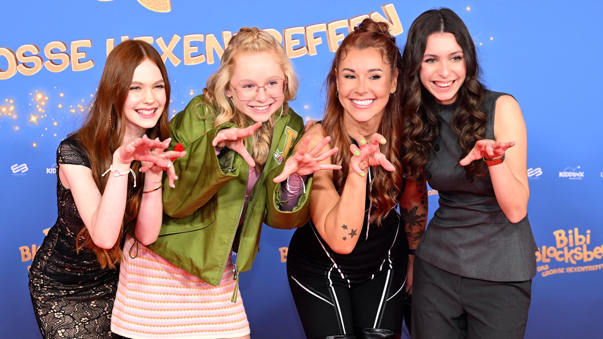 Die jungen Schauspielerinnen Philomena Amari, Nala Langenbach, Tiger Kirchharz und Carla Demmin stehen vor einem Kinoplaket von "Bibi Blocksberg - Das große Hexentreffen".