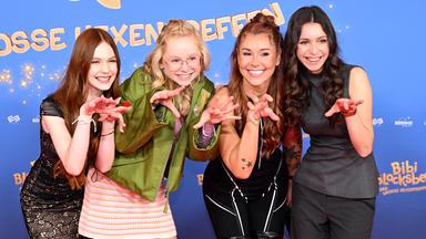 Die jungen Schauspielerinnen Philomena Amari, NALA, Tiger Kirchharz und Carla Demmin stehen vor einem Kinoplaket von "Bibi Blocksberg - Das große Hexentreffen".