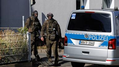 Zwei Polizisten in voller Montur neben einem Polizeiauto