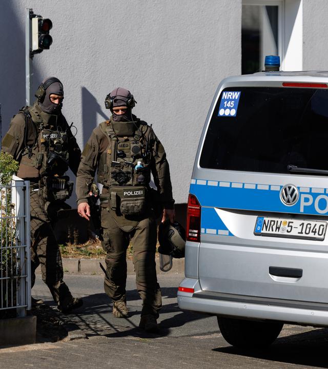 Zwei Polizisten in voller Montur neben einem Polizeiauto