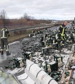 Mehrere Feuerwehrleute in Schutzanzügen räumen auf der Bundesstraße 93 bei Zwickau zahllose zerbrochene Bierflaschen und umgestürzte Getränkekisten von der Fahrbahn. Im Hintergrund stehen Lastwagen und Polizeiabsperrungen. Die Straße ist übersät mit Glasscherben und Getränkeresten, der Verkehr steht still.