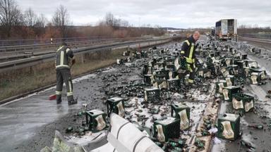 Mehrere Feuerwehrleute in Schutzanzügen räumen auf der Bundesstraße 93 bei Zwickau zahllose zerbrochene Bierflaschen und umgestürzte Getränkekisten von der Fahrbahn. Im Hintergrund stehen Lastwagen und Polizeiabsperrungen. Die Straße ist übersät mit Glasscherben und Getränkeresten, der Verkehr steht still.