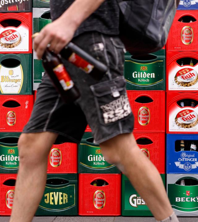 Ein Kunde läuft mit Bierflaschen in der Hand an Bierkästen vorbei