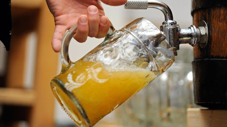 Symbolbild: Ein Mann zapft Bier aus einem Fass in ein Glas
