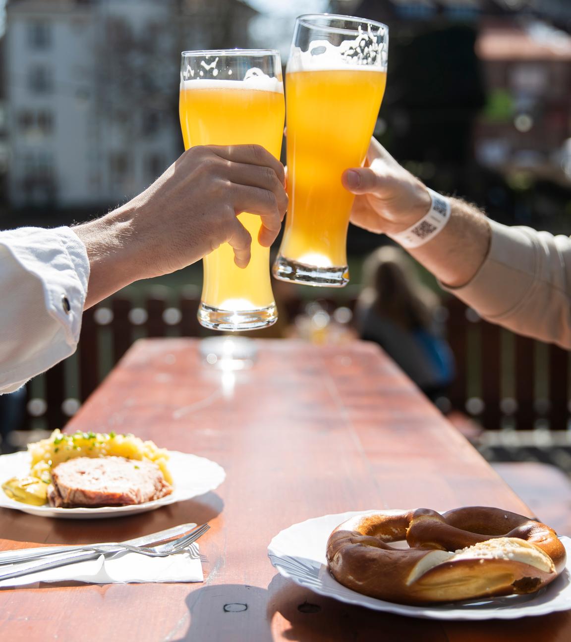 28.03.2021, Baden-Württemberg, Tübingen: Zwei Menschen sitzen bei gutem Wetter in einem Biergarten und stoßen mit einem Bier an.