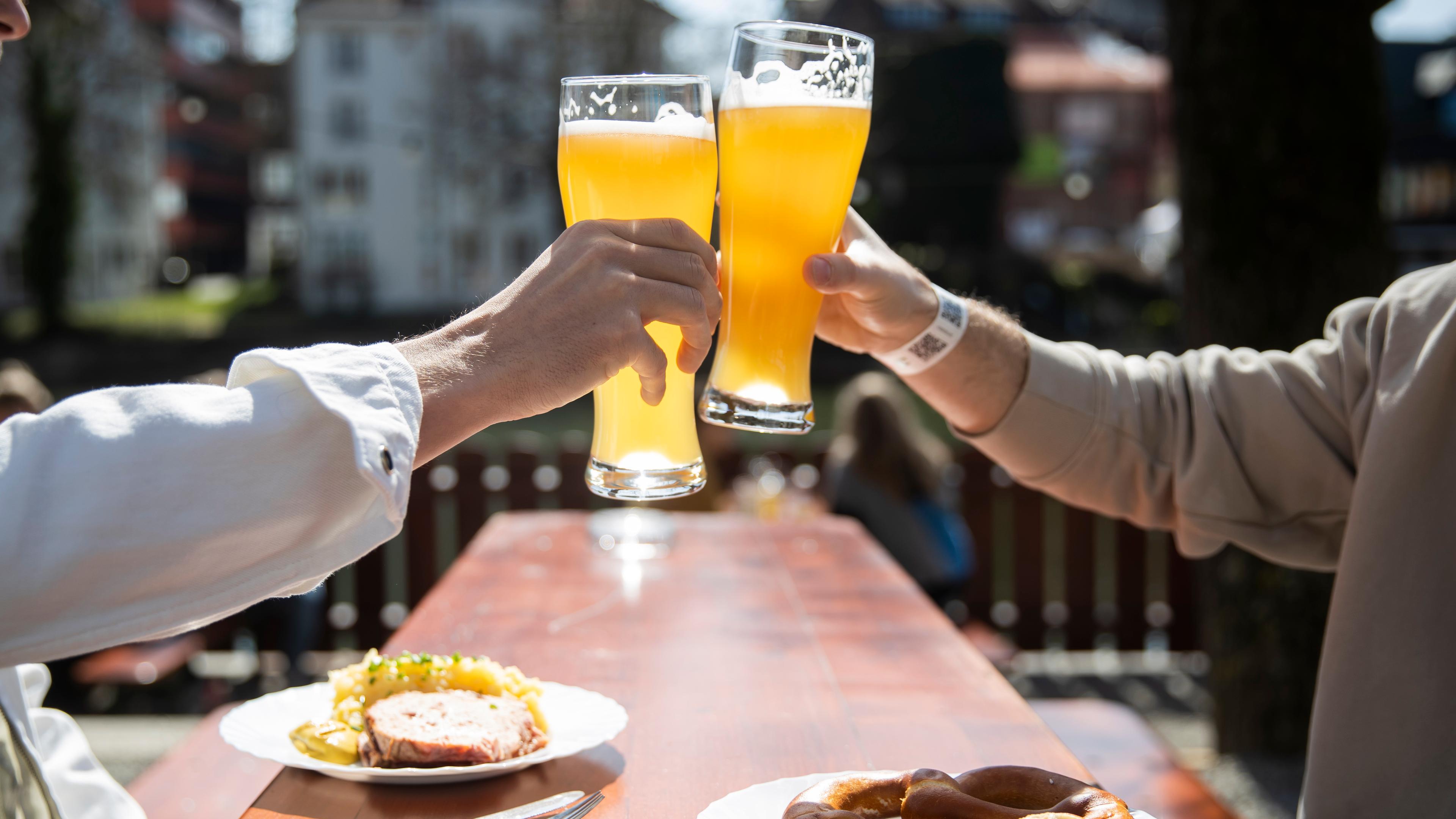 28.03.2021, Baden-Württemberg, Tübingen: Zwei Menschen sitzen bei gutem Wetter in einem Biergarten und stoßen mit einem Bier an.