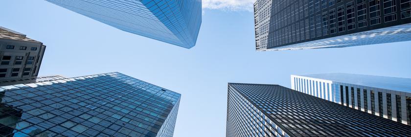 Untersichtiger Blick auf vier Hochhäuser, darüber blauer Himmel.