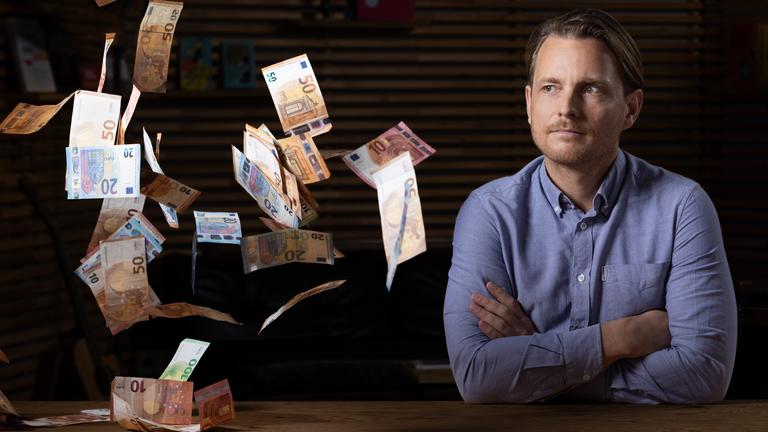 Junger Mann schaut in die Kamera, Geld fliegt umher.