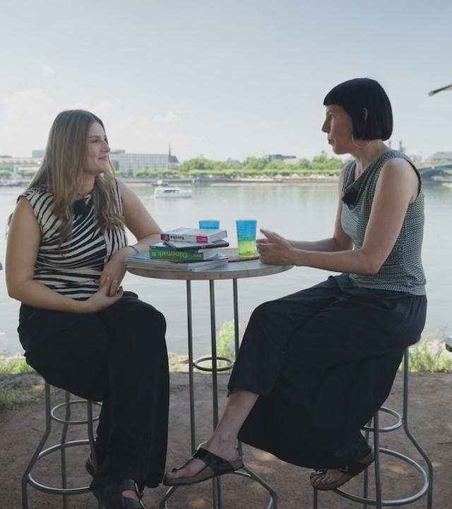 Zwei Frauen sitzen an einem Tisch und unterhalten sich.