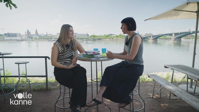 Zwei Frauen sitzen an einem Tisch und unterhalten sich.