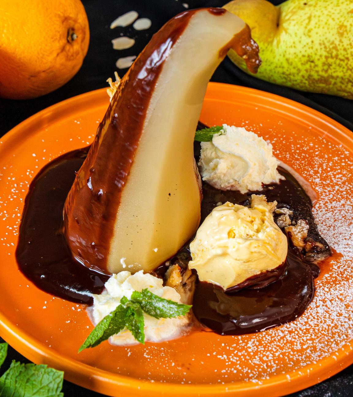 Pochierte Birne auf orangenem Teller mit Schokoladensauce und Schlagsahne
