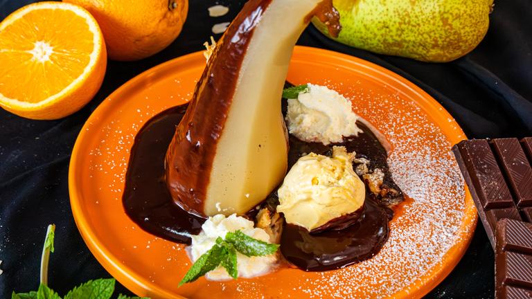 Pochierte Birne auf orangenem Teller mit Schokoladensauce und Schlagsahne