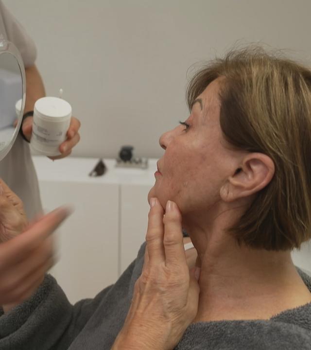 Eine Frau hält einen Handspiegel und betrachtet ihr Spiegelbild.