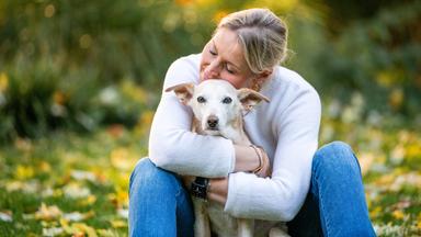 Carmen umarmt Hund Mila. Sie sitzen auf einer Wiese. 