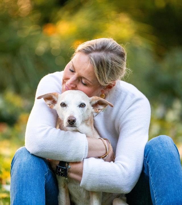 Carmen umarmt Hund Mila. Sie sitzen auf einer Wiese. 