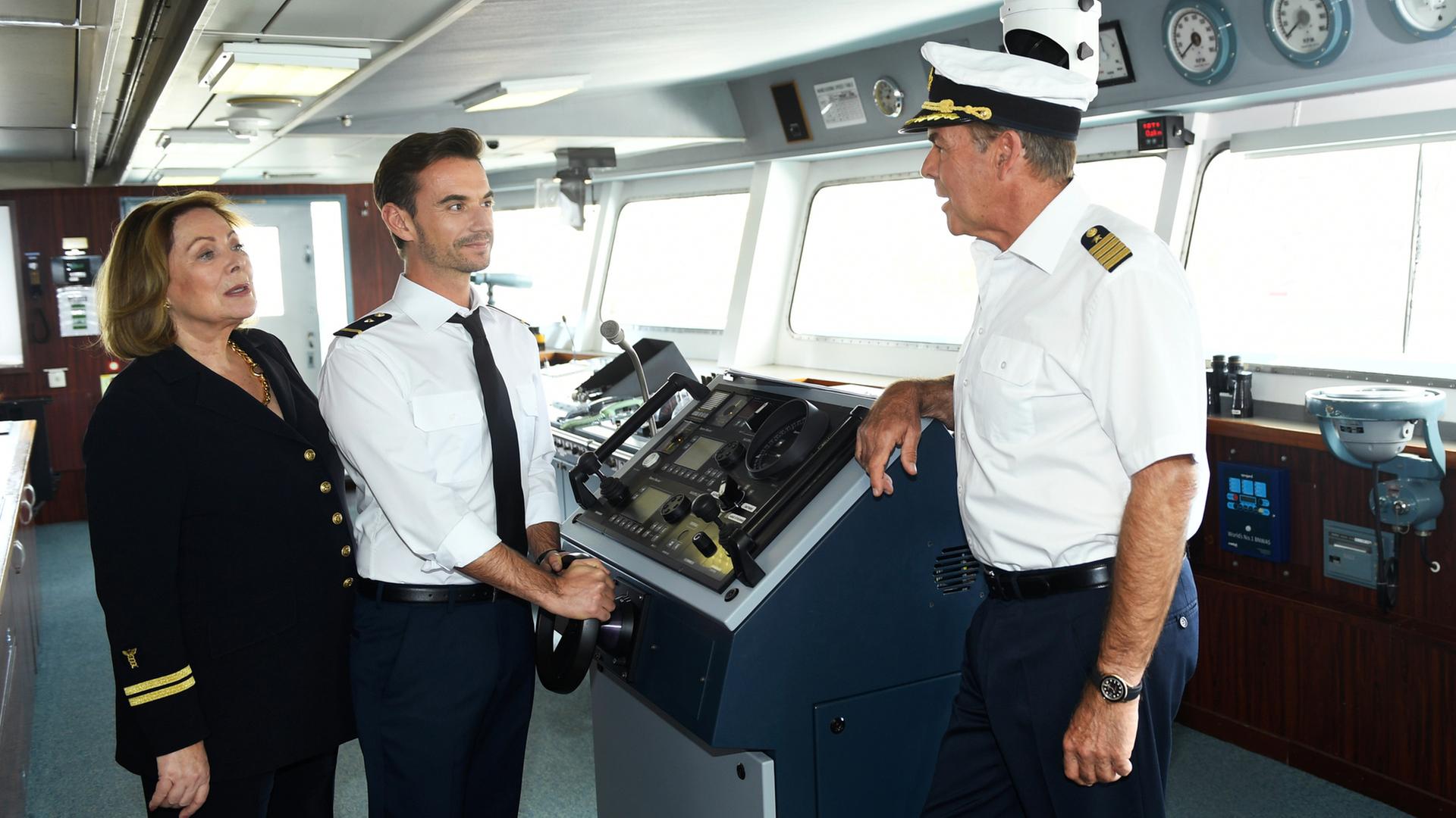 "Das Traumschiff: Tansania": Der junge Offizier Florian (Florian Silbereisen) steht am Ruder des Schiff-Steuerraums und lächelt Kapitän Burger (Sascha Hehn) an, der ihm gegenüber steht und mit ihm redet. Neben Florian steht Beatrice (Heide Keller).