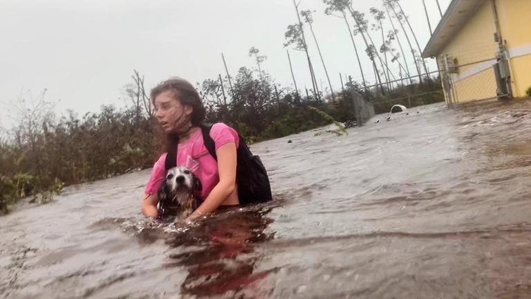 Julia Aylen watet mit ihrem Hund durch hüfthohes Wasser auf einer überfluteten Strasse, aufgenommen am 03.09.2019 in Freeport (Bahamas)